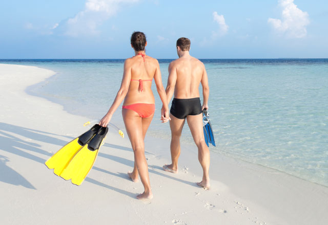 Couple carrying flippers along a stretch of sandy beach